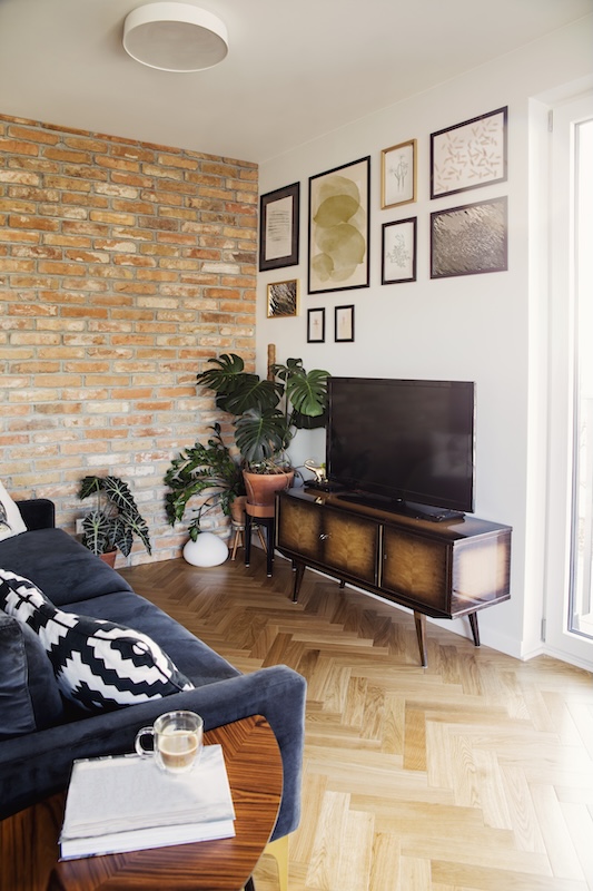 granatowa kanapa obok ceglanej ściany salon z kanapą przed telewizorem i ceglaną ścianą